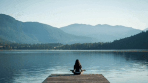 A woman meditating on a wooden dock by a calm lake, showing how willpower and self-control support inner peace.