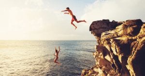 Couple jumping from cliff into the ocean