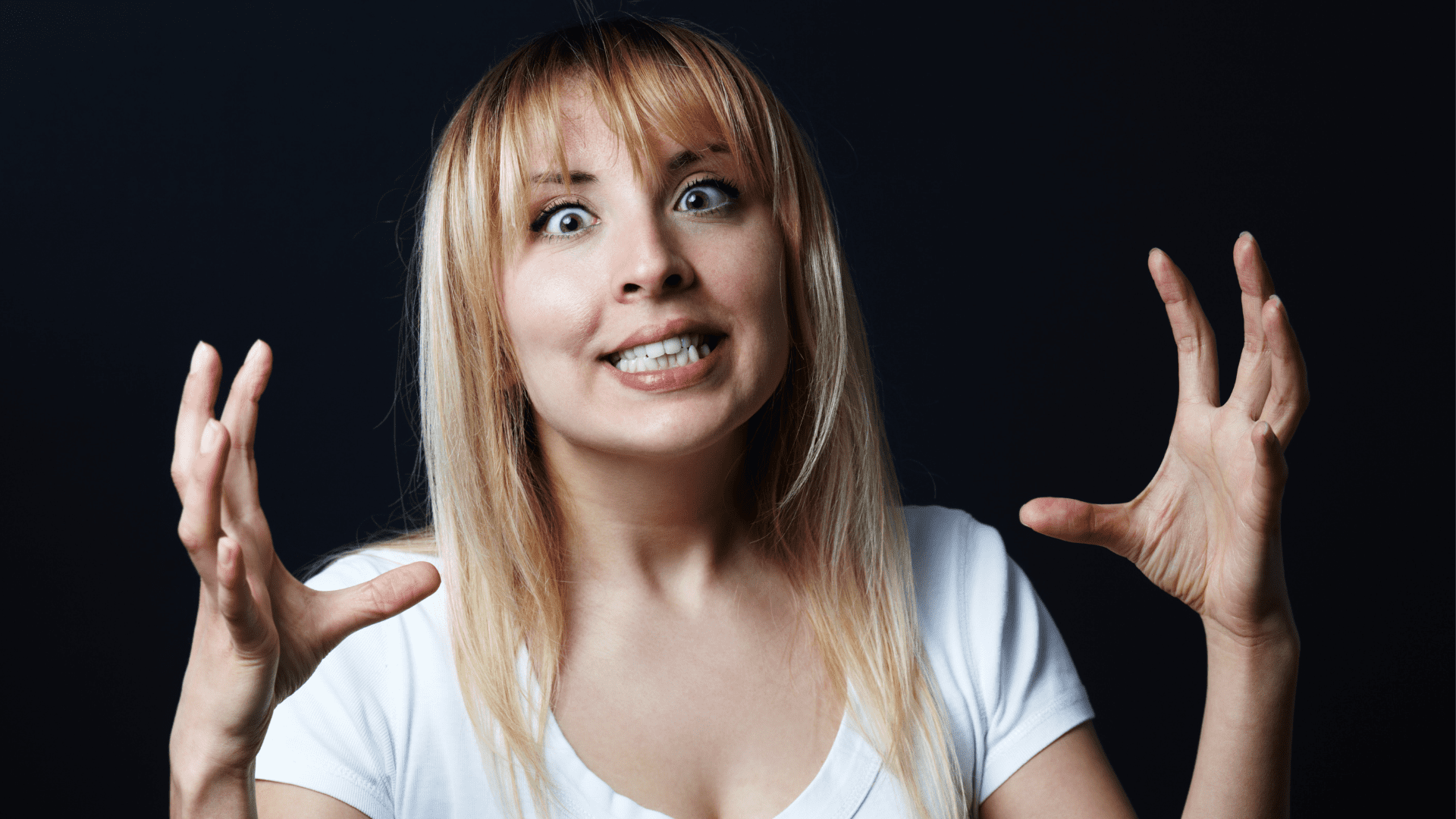 Angry woman with wide eyes and raised hands expressing surprise or shock.