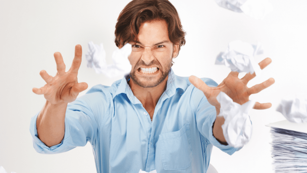 Man with angry expression throwing crumpled papers.