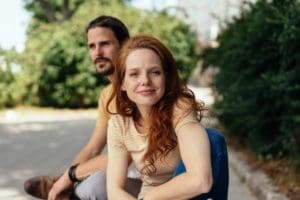 Young woman leaning towards the camera with an attentive expression and friendly smile outdoors with her boyfriend
