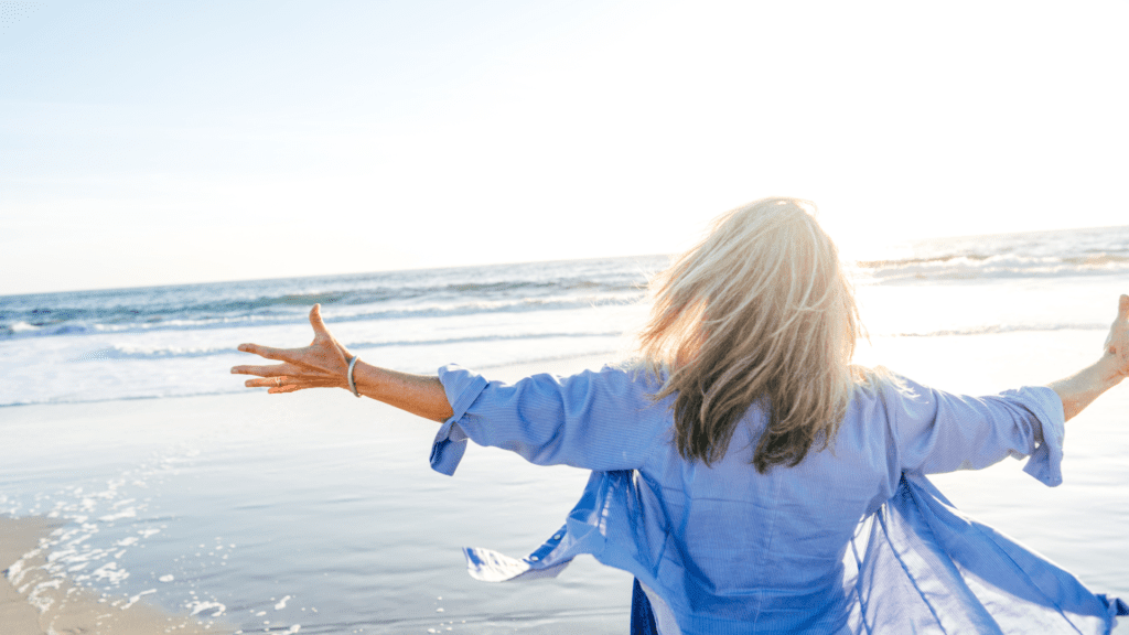 Joyful woman with arms spread at the beach, symbolizing emotional well-being, self-improvement, and understanding emotions for mental well-being