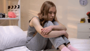 Image of a young woman sitting on her bed, holding her head in her hands, expressing symptoms of anxiety. This image relates to the topic of anxiety and the benefits of brain-based coaching and neuroplasticity in managing anxiety. Brain-Based Coaching Techniques