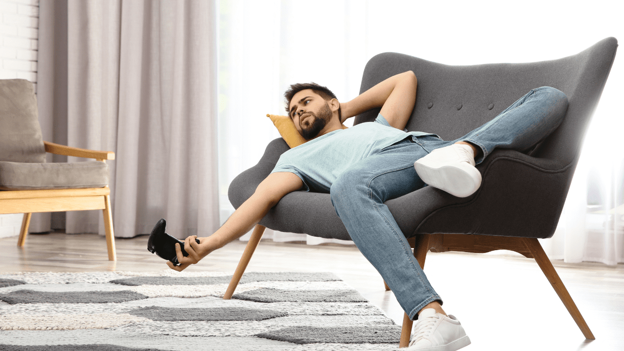 Man laying on a chair with a video game controller, highlighting the need for self-motivation strategies and goal setting for success, self-driving goal