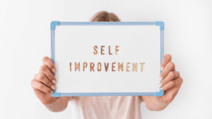 A woman holding up a whiteboard with the words "Self Improvement" in gold letters and a blue border. The image represents the concept of self-improvement and personal growth through brain-based life and performance coaching with Dr. Sydney Ceruto.