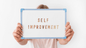 A woman holding up a whiteboard with the words "self improvement" in gold letters and a blue border. The image represents the concept of self-improvement and personal growth through brain-based life and performance coaching with dr. Sydney ceruto.