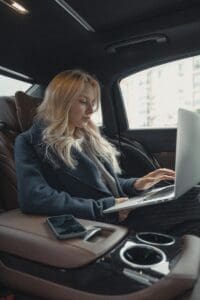 Woman in gray business suit inside a luxurious car, working on laptop, exemplifying leadership from neuroscience-based executive coaching.