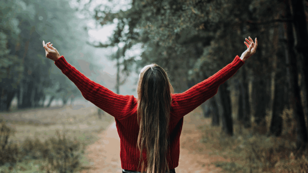 Neuroplasticity and Cognitive Restructuring 4 Woman in a red sweater with arms raised in nature, symbolizing freedom through neuroplasticity and cognitive restructuring.
