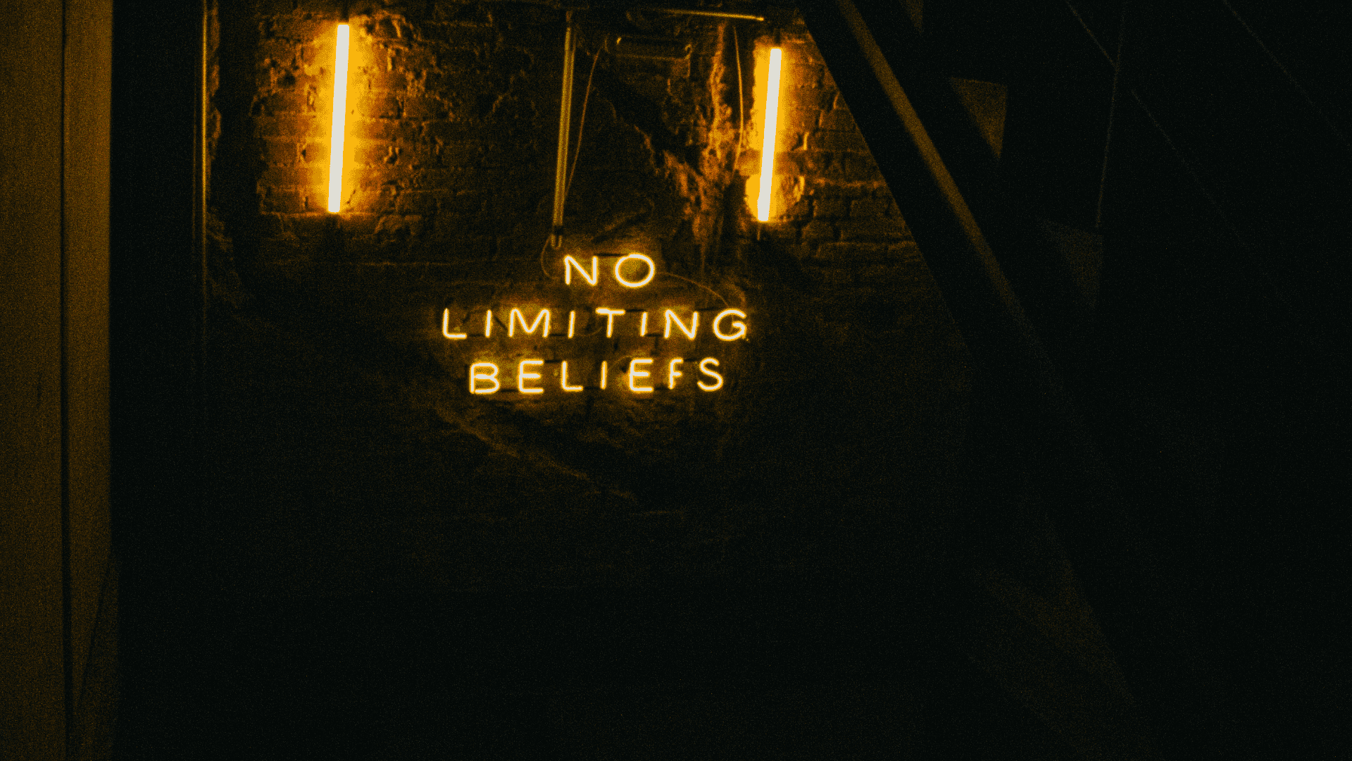 Neon sign with the words "No Limiting Beliefs" illuminated against a dark brick wall.