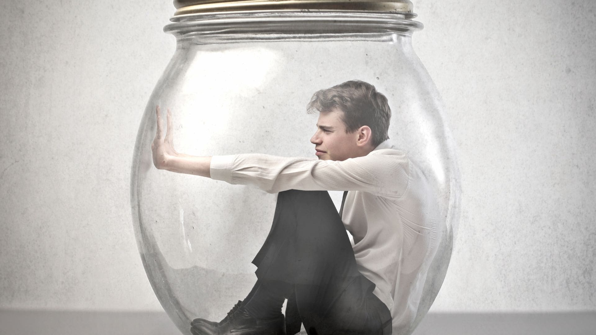 Man trapped inside a glass jar, pushing against the walls from his own mind traps.