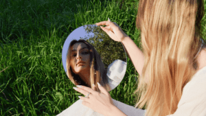 Woman on grass with mirror experiencing self-awareness moment