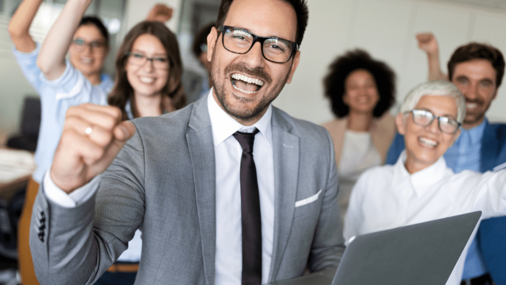 Group of business professionals celebrating success with raised fists and smiles.