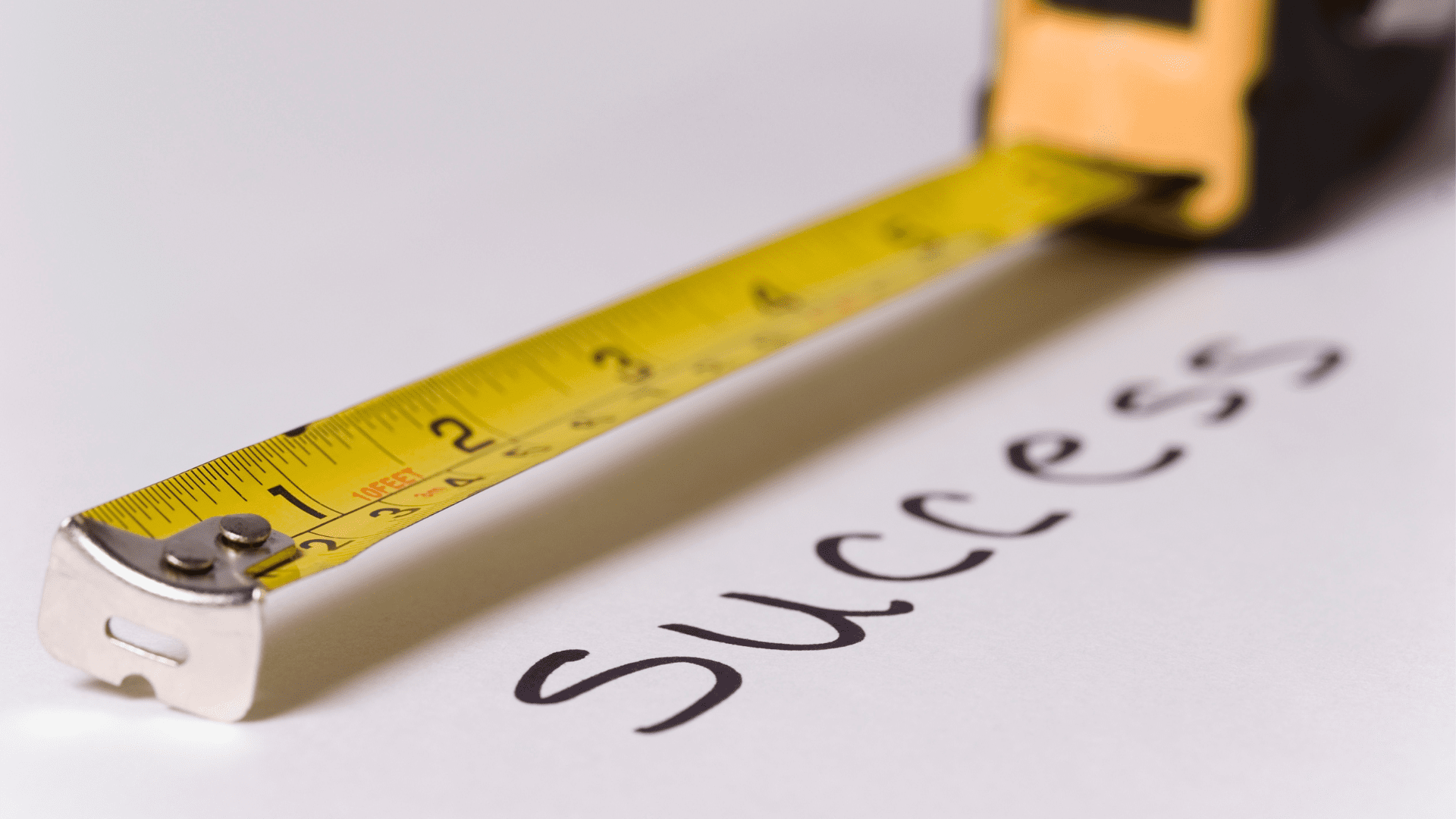 Close-up of a measuring tape extended over the word 'Success' written on paper.