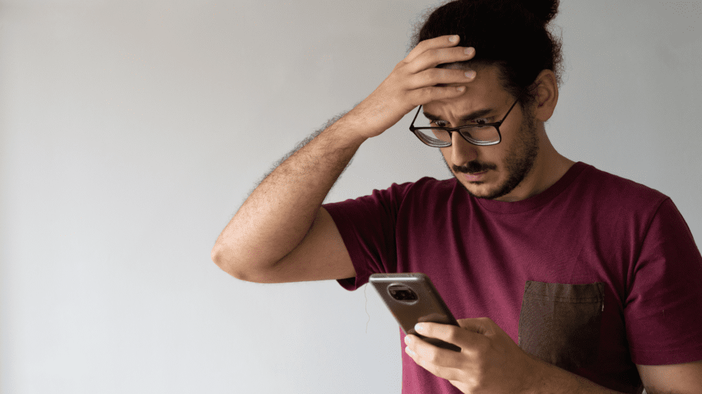 a man holding his head looking at a cellphone feeling anxious