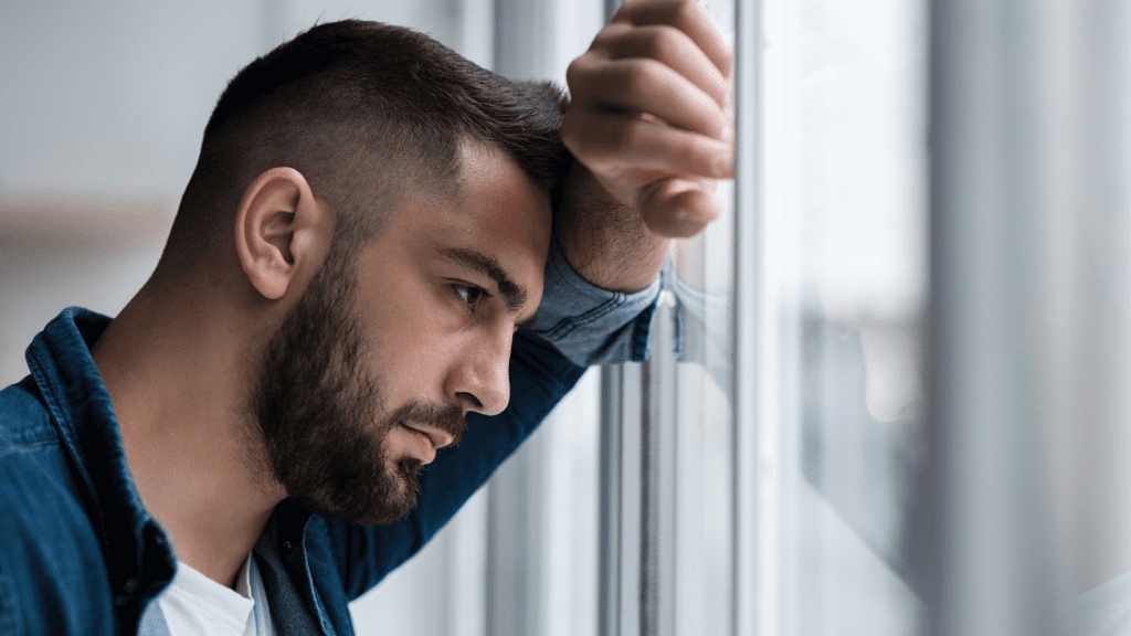 a man leaning against a window feeling lonely and trying to understand feeling of loneliness