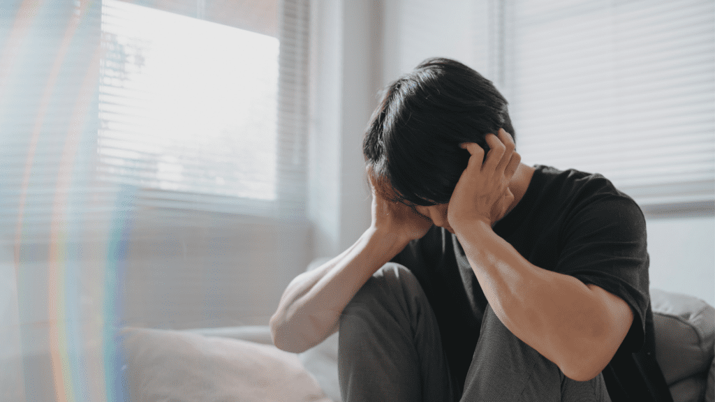 young man with dark hair holding his head in his hands