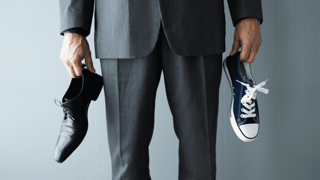 a man holding one work shoe and one sneaker