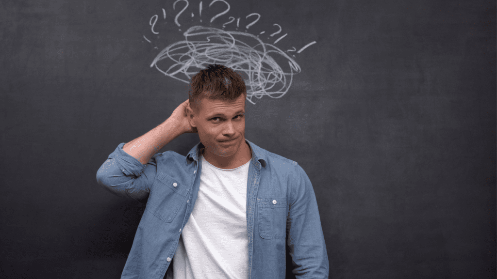 Man scratching his head with confused expression and question marks above his head representing self-doubt.
