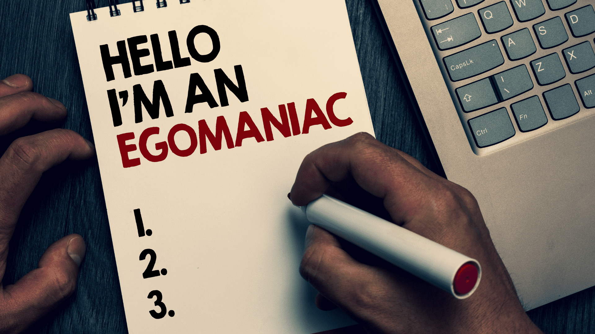 Notebook with "Hello I'm an Egomaniac" written on it next to a laptop referencing narcissism.