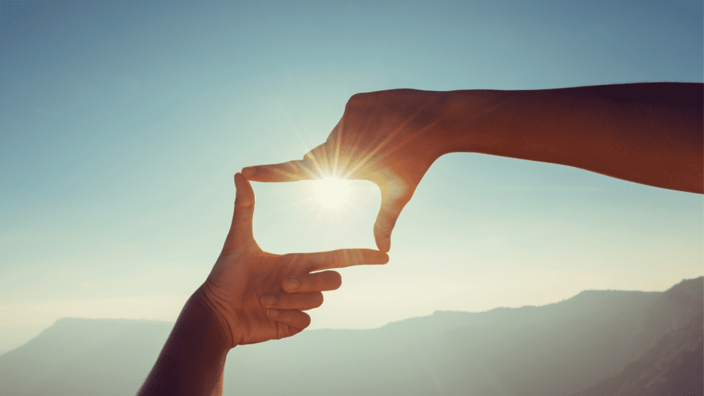 Hands framing the sun with a scenic background, symbolizing changing perspective.