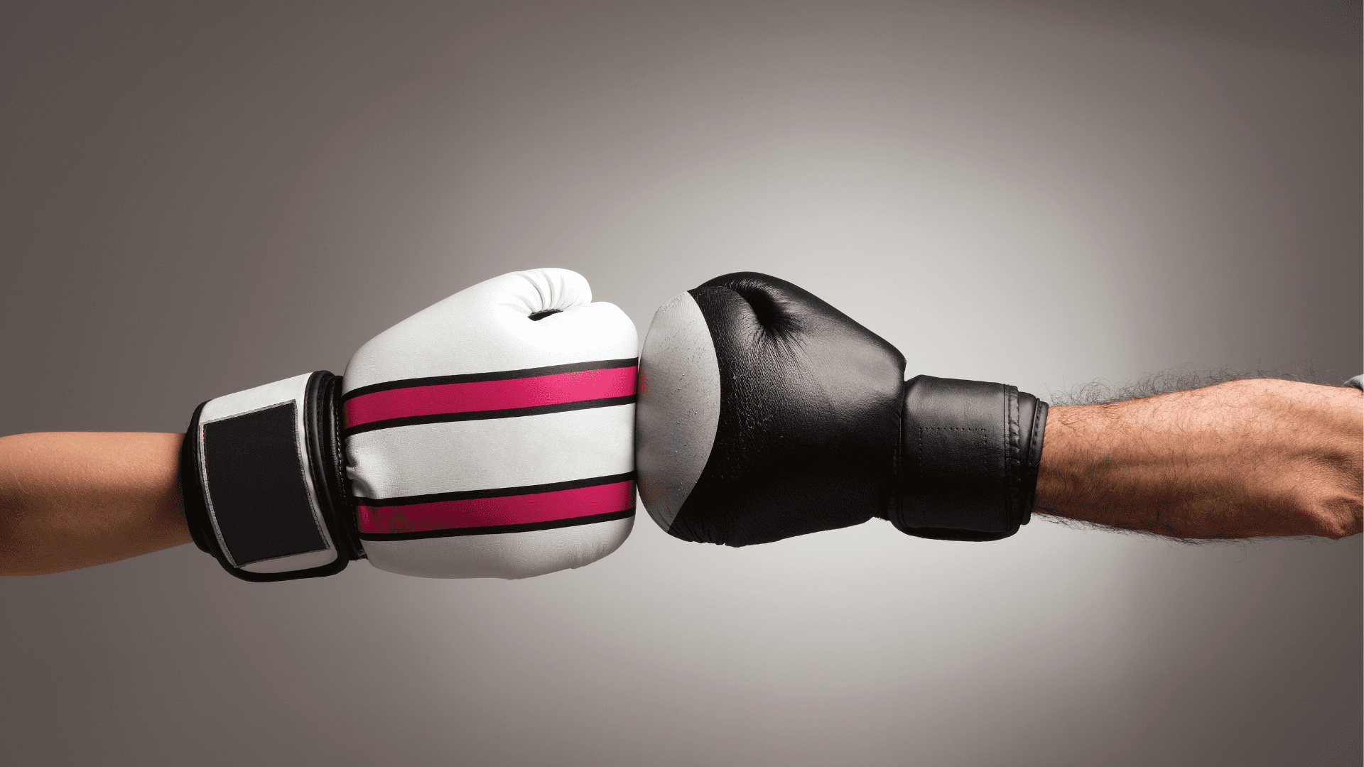 Two boxing gloves, one black and one white with pink stripes, meeting in a fist bump, symbolizing constructive conflict.