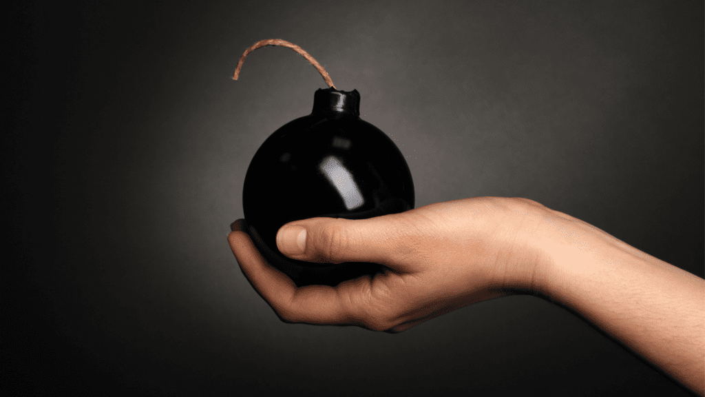 A hand holding a black bomb with a wick indicating someone who self-sabotages.