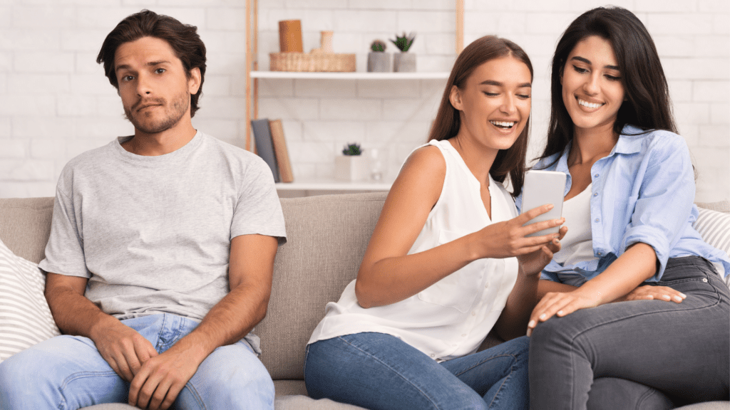 Man sitting apart from two women on a couch, illustrating codependent dynamics.