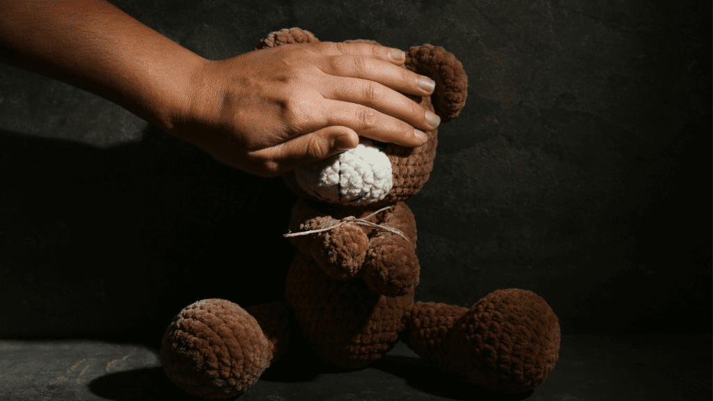 Hand covering a teddy bear's face symbolizing childhood trauma.