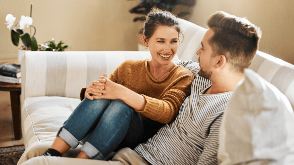 Couple smiling and talking on a couch, showcasing open communication.
A couple sitting together on a couch, exemplifying the emotionally feral approach with genuine smiles and open body language.