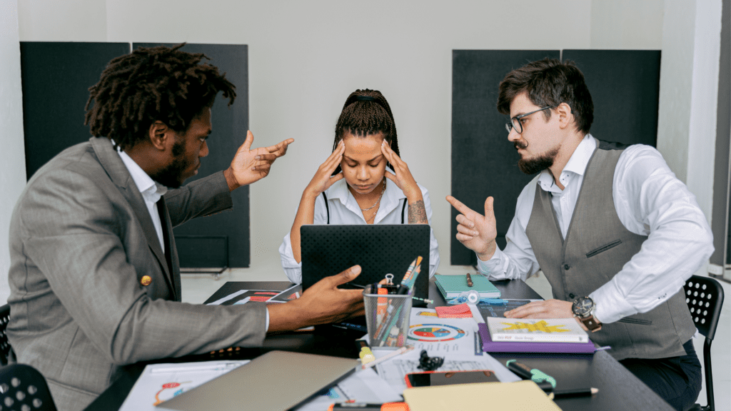 Confrontation during a meeting, showcasing a woman holding her temples with her hands during a confrontation between two male colleagues.
