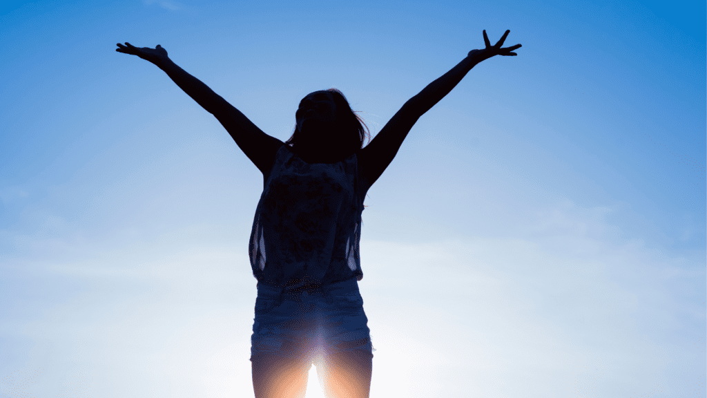 Silhouette of a person with arms outstretched against a blue sky