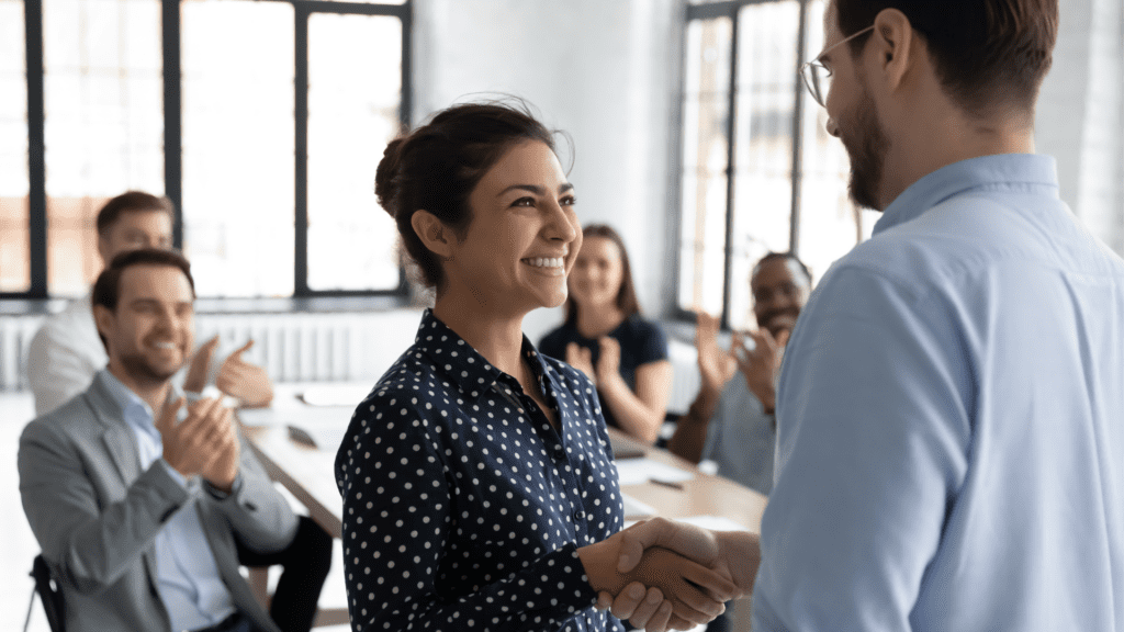 Smiling woman receiving a handshake and applause at work"
