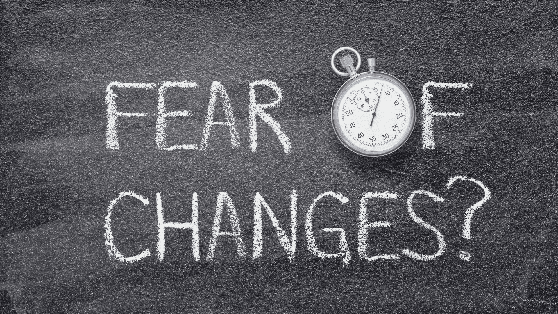 "Fear of change" written on a chalkboard next to a stopwatch, symbolizing the urgency of overcoming resistance to change.