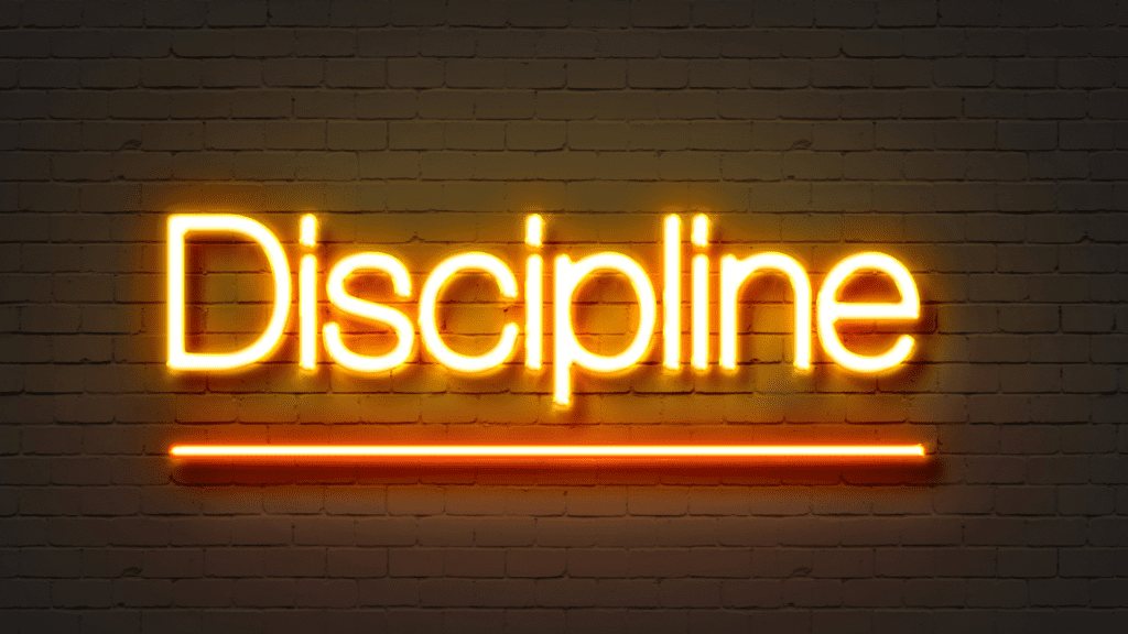 Neon sign with the word "Discipline" glowing on a dark brick wall



