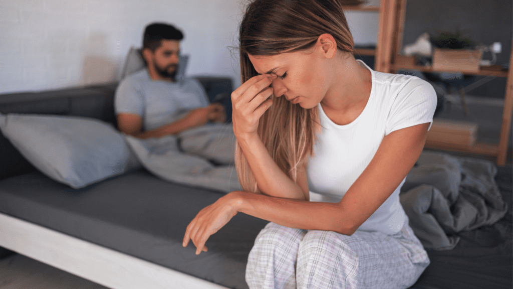 Woman sitting on bed looking distressed, indicating relationship struggles.

