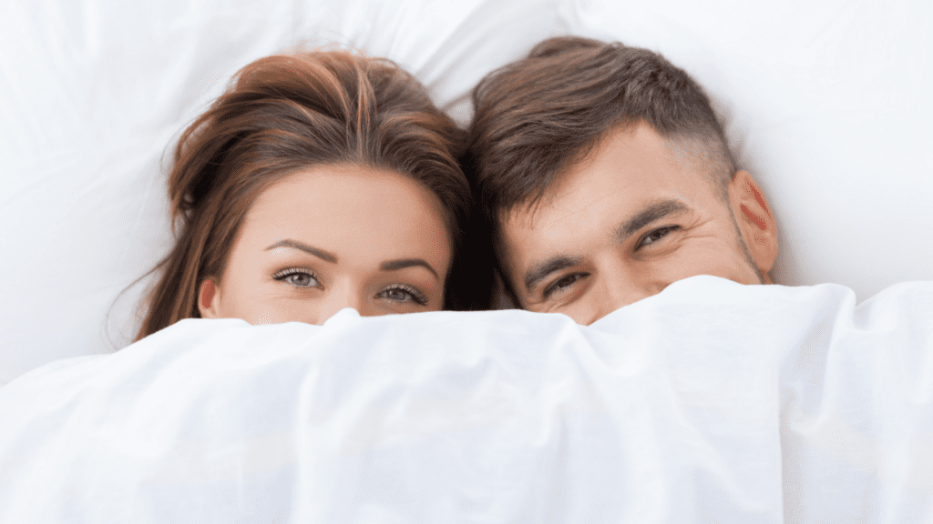 Couple smiling under a blanket, symbolizing intimacy and connection.

