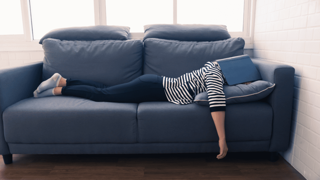 Person lying on a couch with a book covering their face, representing avoidance behavior.


