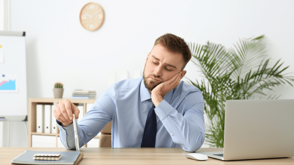 Man sitting at a desk appearing bored
Alt: Businessman sitting at a desk looking bored and unmotivated.

