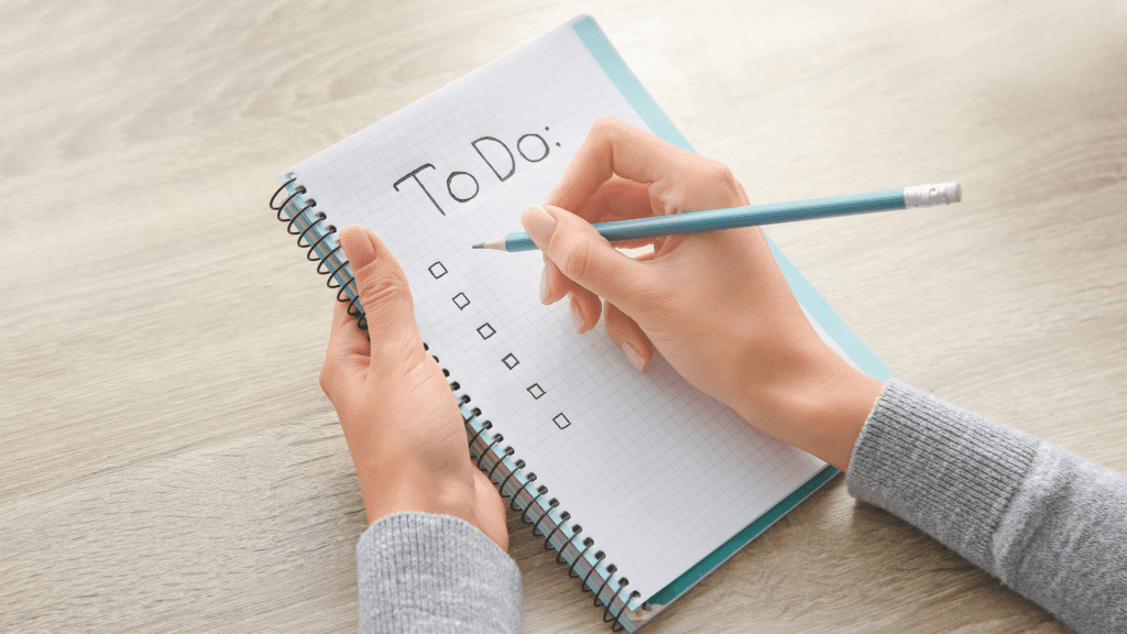 Person writing on a spiral notebook with to-do list checkboxes
