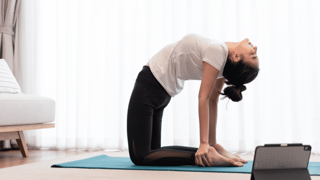 Woman practicing camel pose yoga at home with tablet



