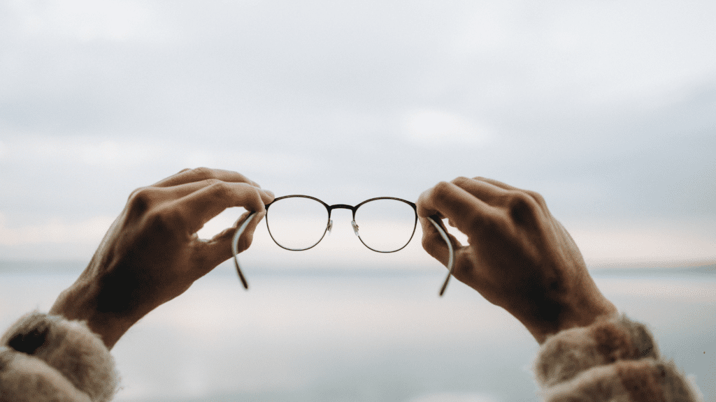 Hands holding eyeglasses against blurred horizon background


