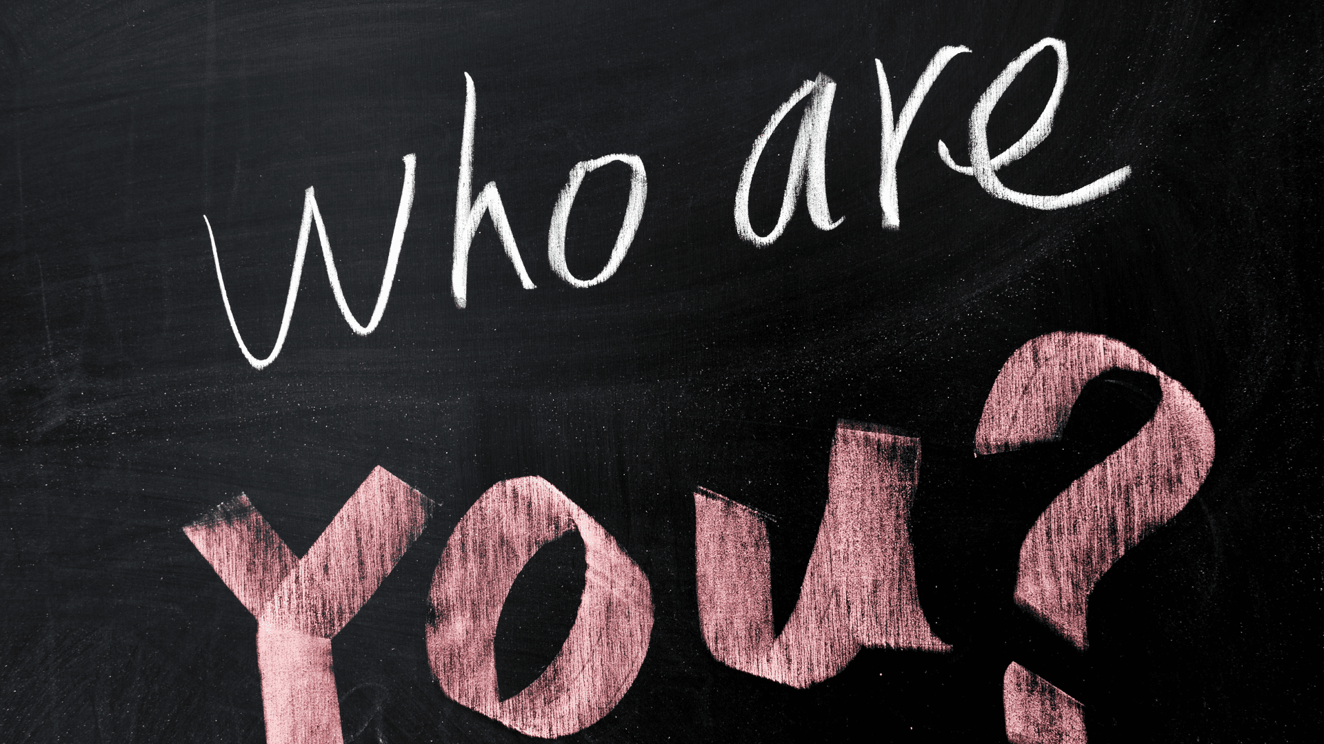 Chalkboard with white text reading "Who are" and pink text reading "you" against a black background, representing the question of identity and authenticity