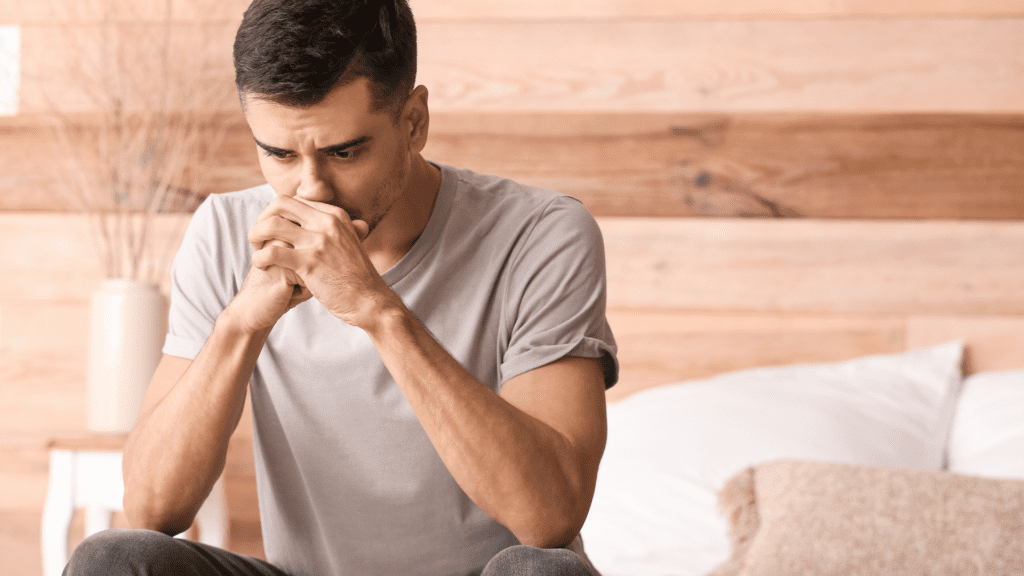 Man in white t-shirt deep in thought with hands clasped


