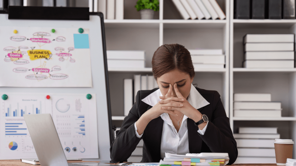 Professional woman experiencing stress at desk with business plan and charts

