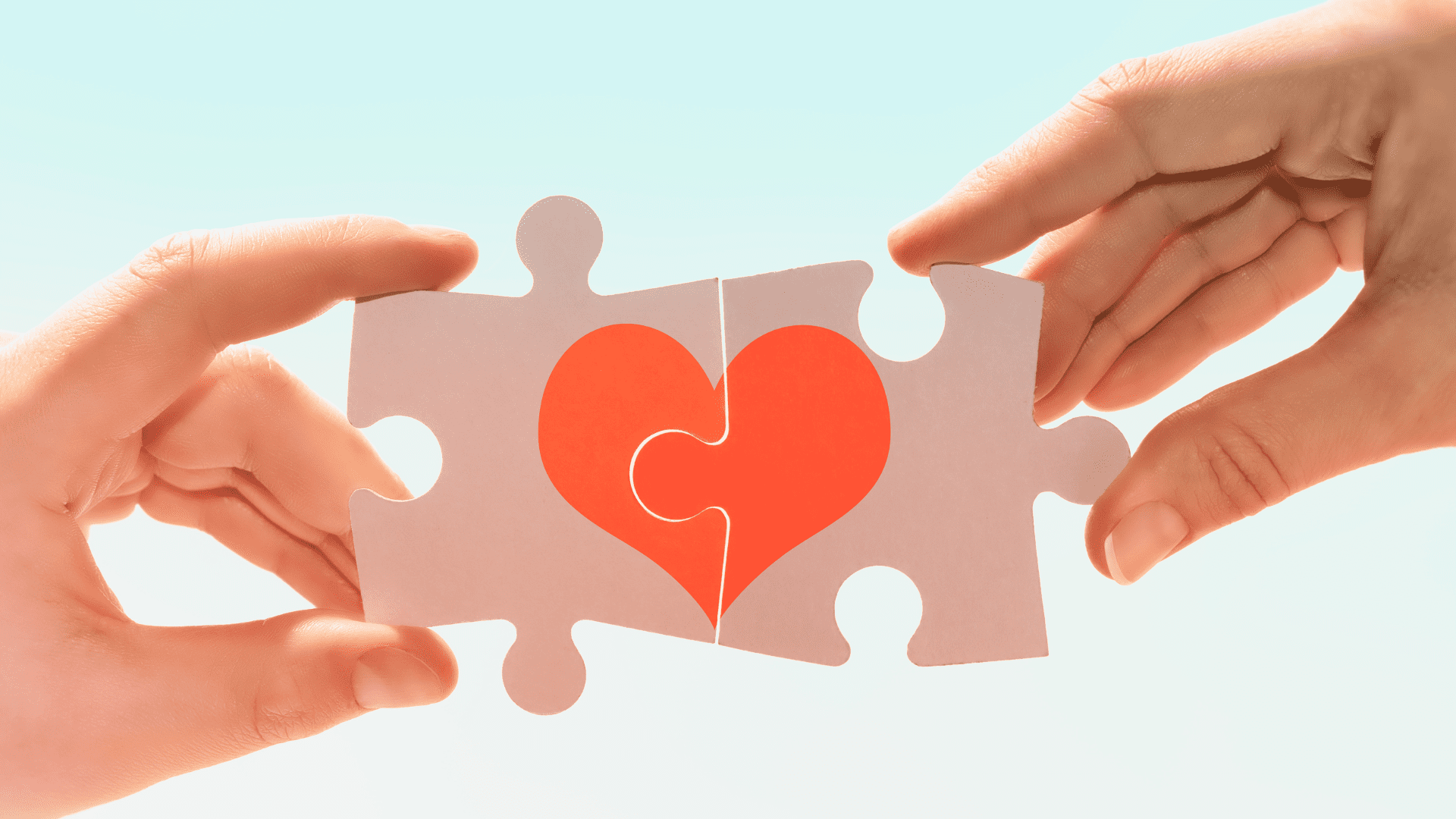 Two hands holding puzzle pieces with a heart in the center, symbolizing relationship compatibility.