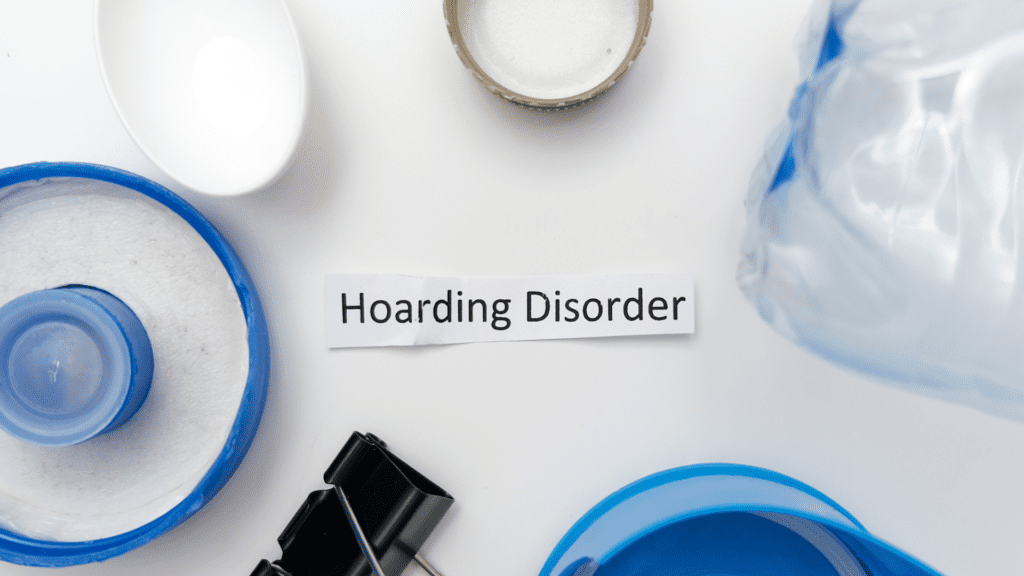 A sign reading "Hoarding Disorder" surrounded by miscellaneous clutter, symbolizing the disorders impact.

