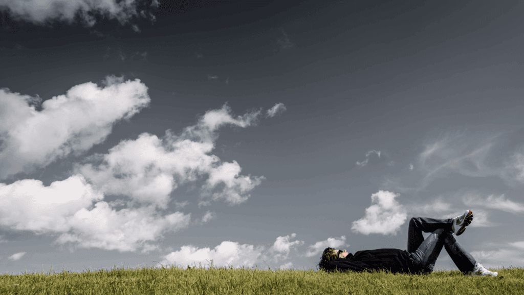A person relaxing on the grass under a sky with both dark and light clouds, symbolizing the transition from rigid thought patterns to cognitive balance.