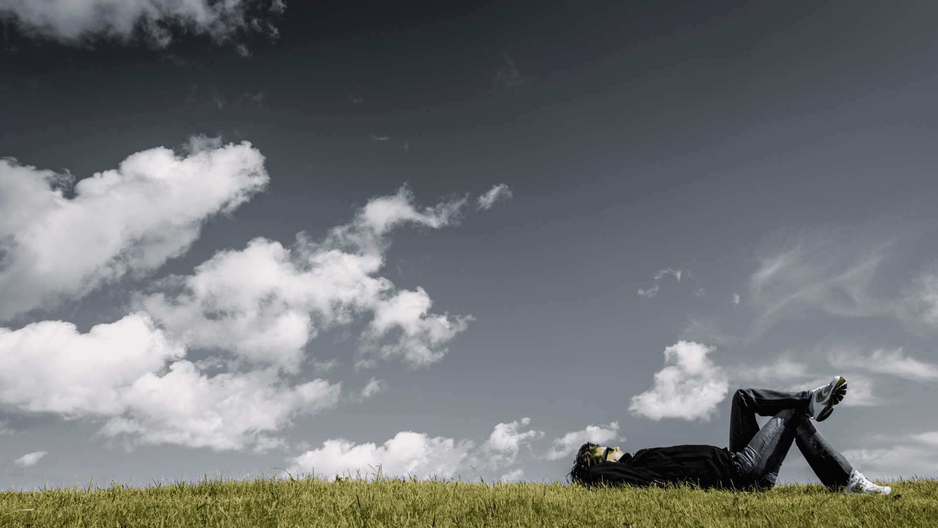 A person relaxing on the grass under a sky with both dark and light clouds, symbolizing the transition from rigid thought patterns to cognitive balance.