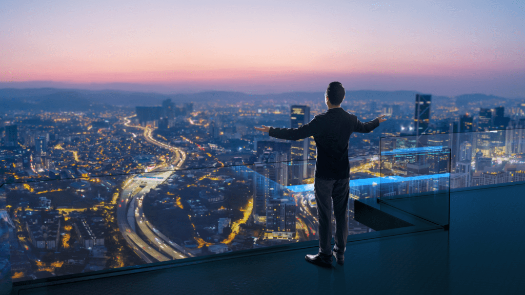  A man standing on a high-rise balcony overlooking a city skyline, symbolizing a visionary mindset and leadership.

