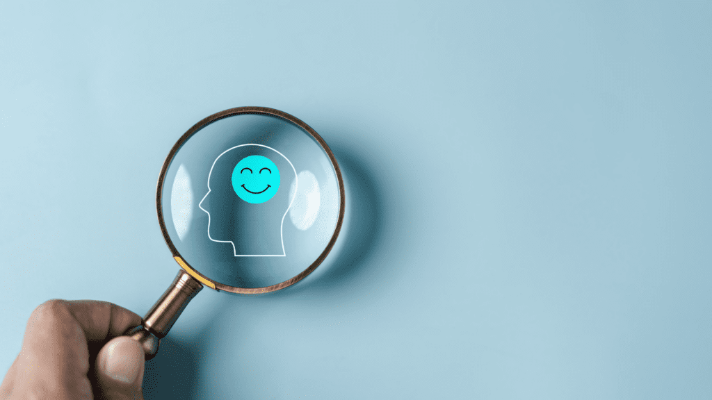A magnifying glass focusing on a smiling brain icon, symbolizing the impact of examples of overgeneralization on your mental health and the importance of cognitive awareness.